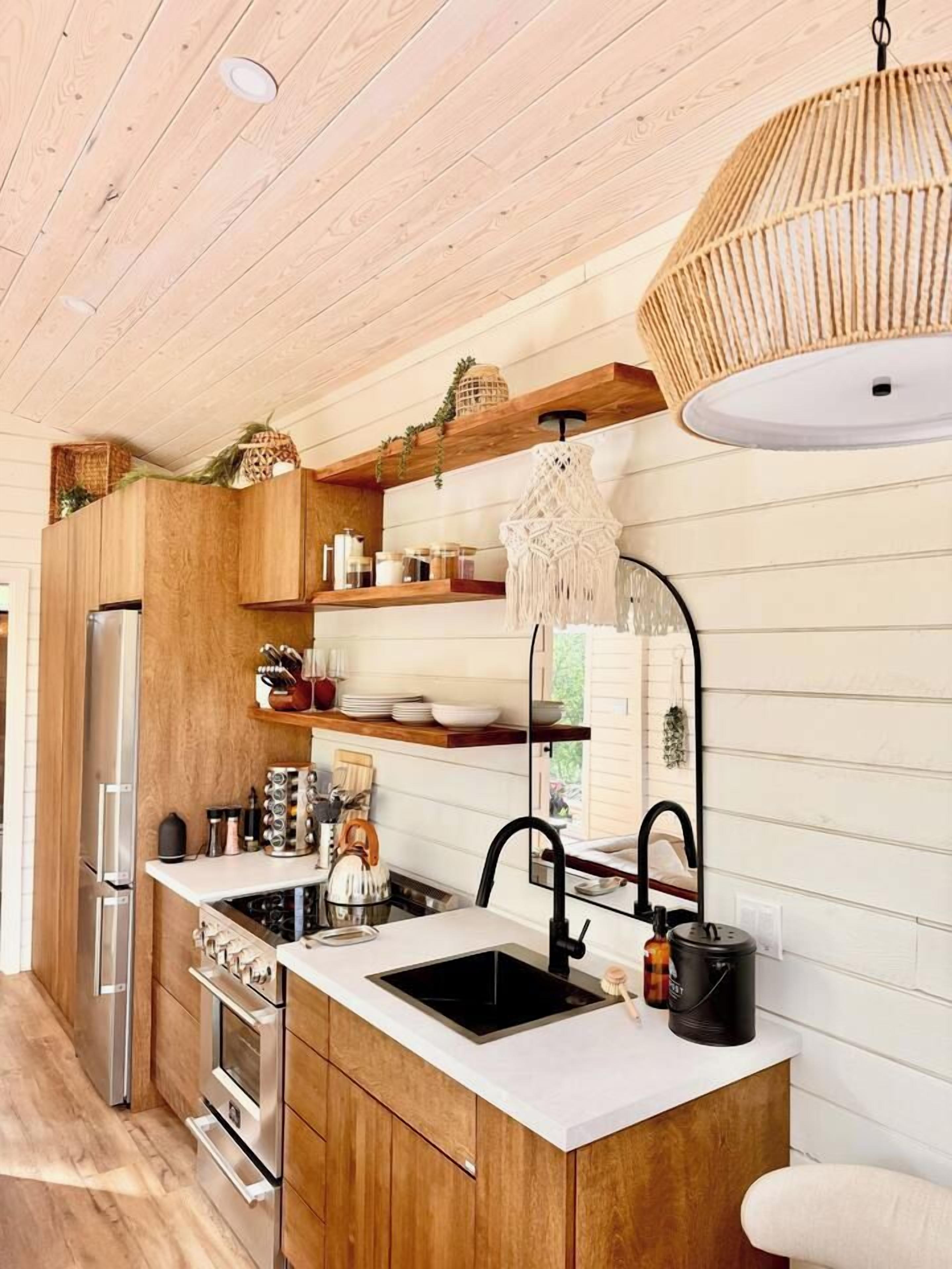 Una cocina moderna con armarios de madera, un refrigerador de acero inoxidable, horno empotrado, encimera blanca y lámpara colgante.