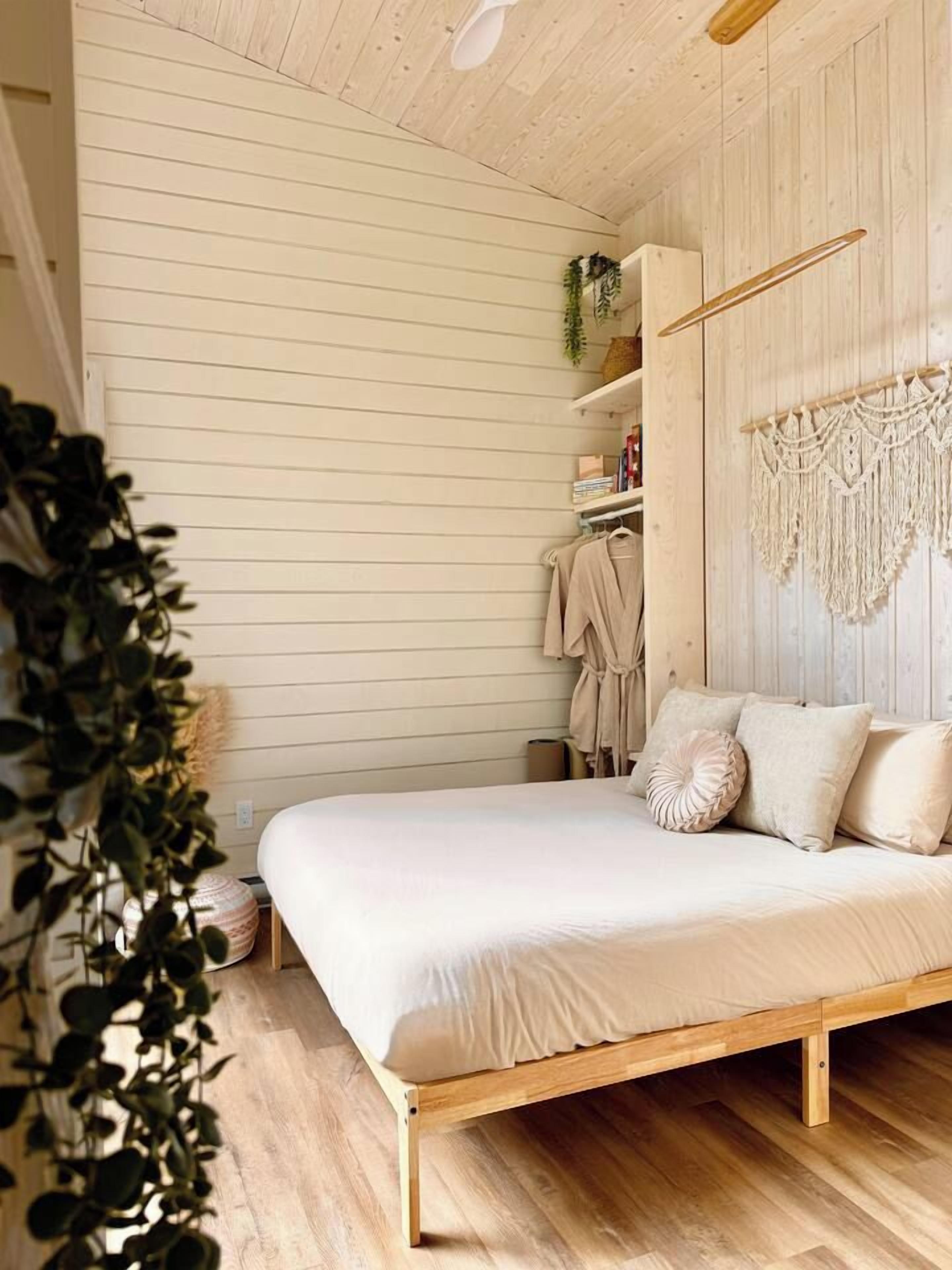 A bedroom with a wooden bed frame, a macrame wall hanging, and a plant.