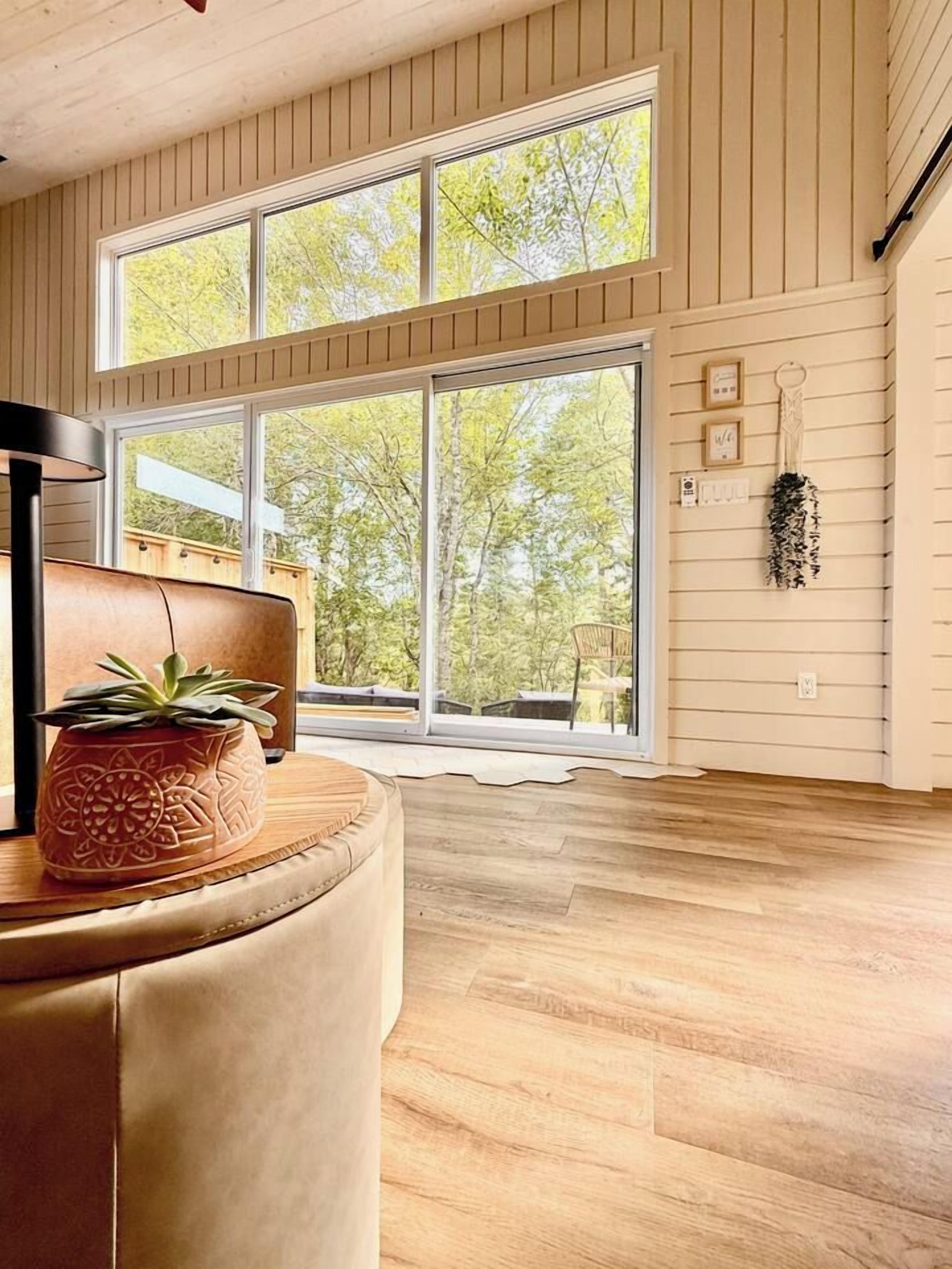 Una habitación amplia con un gran ventanal, una planta en maceta y suelo de madera.