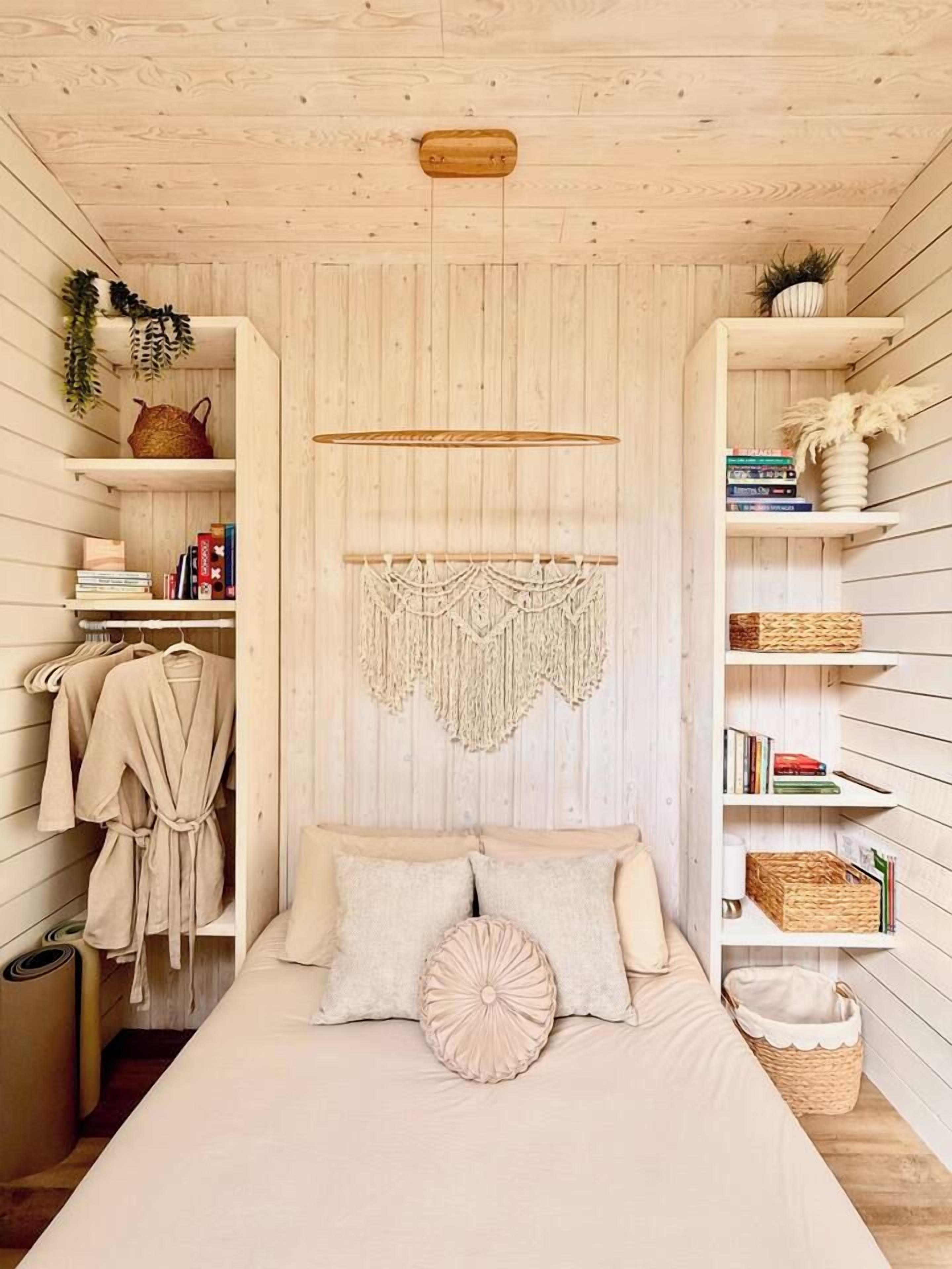Una habitación con cama, un tapiz de macramé, estantes con libros y cestas, y techo de madera.