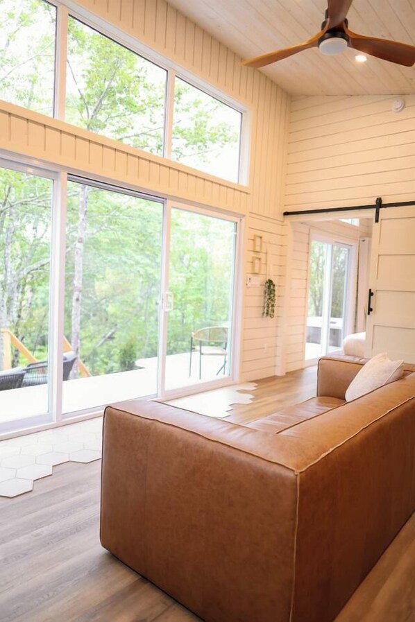 A modern interior with a large window, a ceiling fan, and a brown leather sofa.
