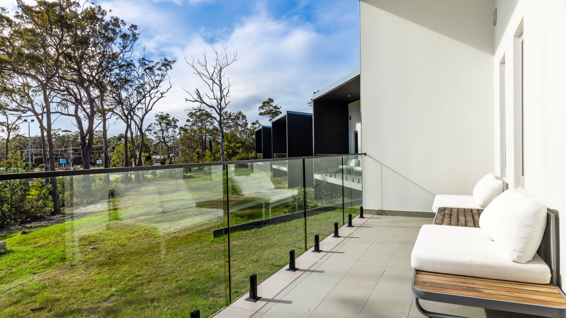 A balcony with a glass railing overlooking a grassy area and trees.