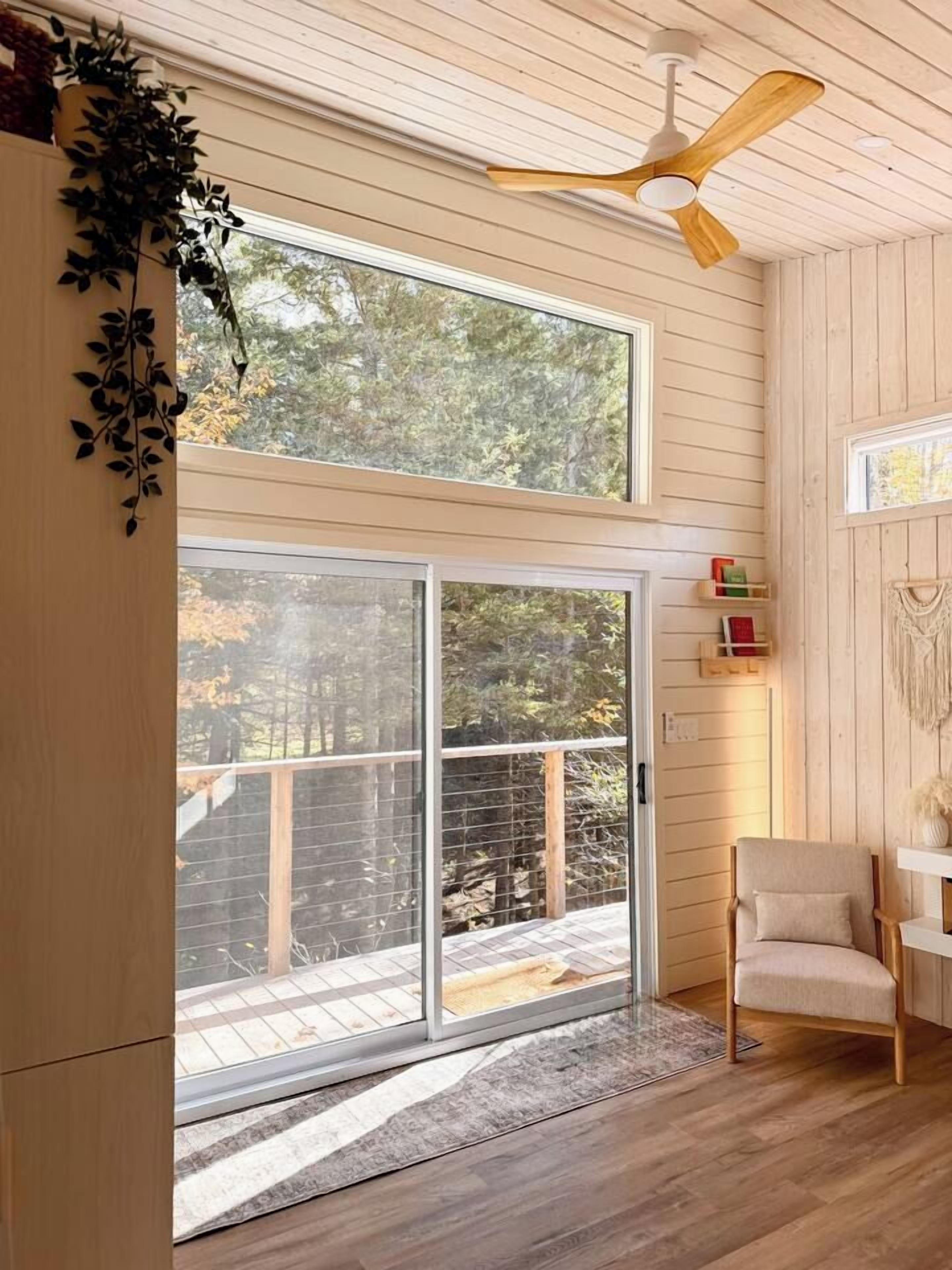 Une pièce dotée d’une grande porte-fenêtre coulissante donnant sur une terrasse, d’un ventilateur de plafond et d’un fauteuil.