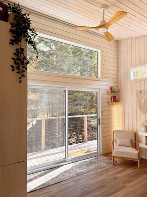 A room with a large sliding glass door leading to a deck, a ceiling fan, and a chair. - Haven Nature Retreat•Shine & Rise Wellness (Sainte-Marie-de-Kent)