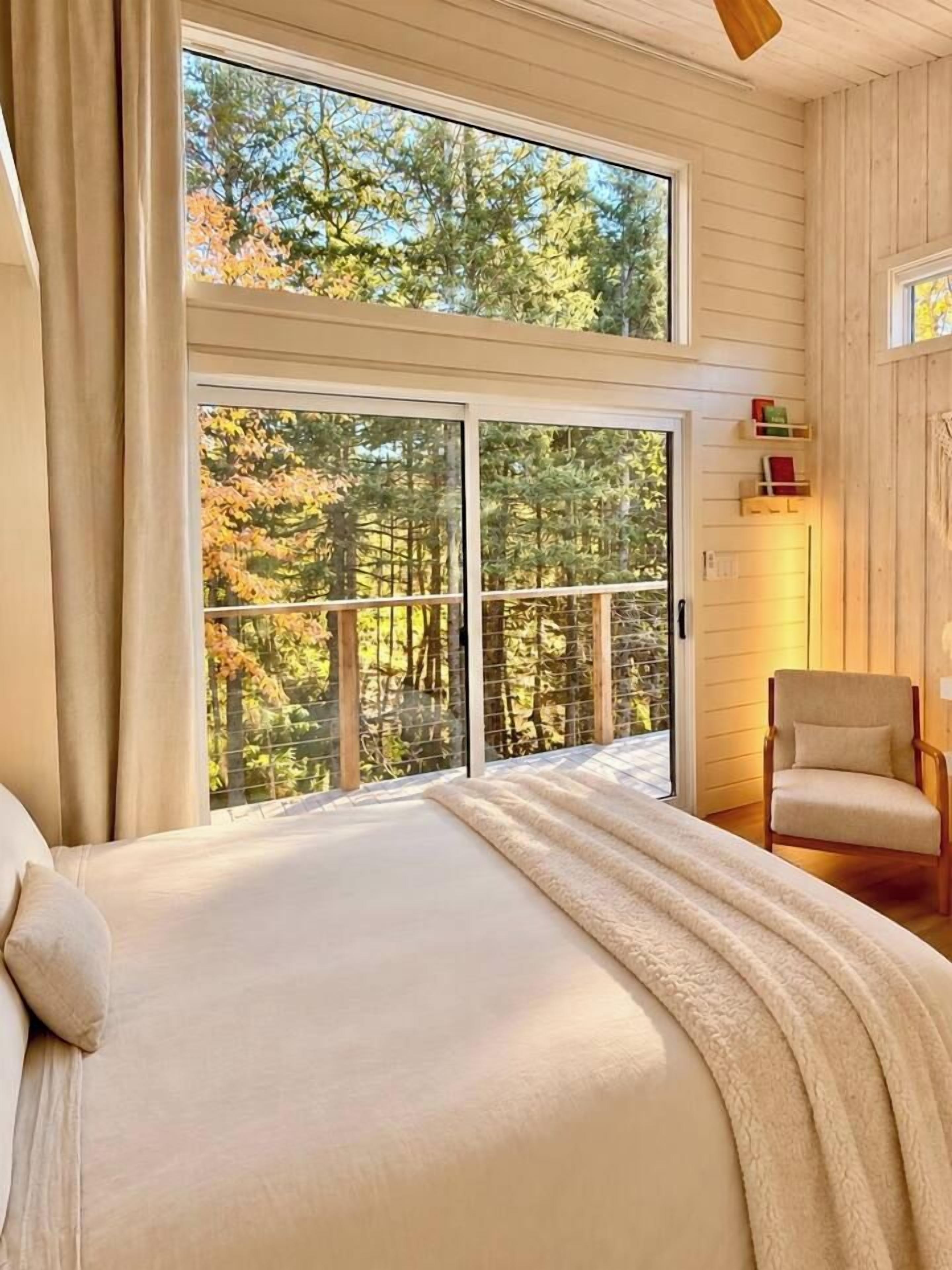 Una camera da letto con un letto grande, una sedia e un balcone che si affaccia su alberi.