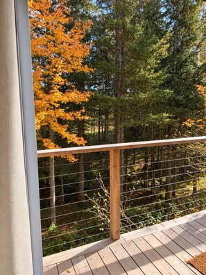 A wooden deck with a metal railing overlooking a forested area with autumn foliage. - Haven Nature Retreat•Shine & Rise Wellness (Sainte-Marie-de-Kent)