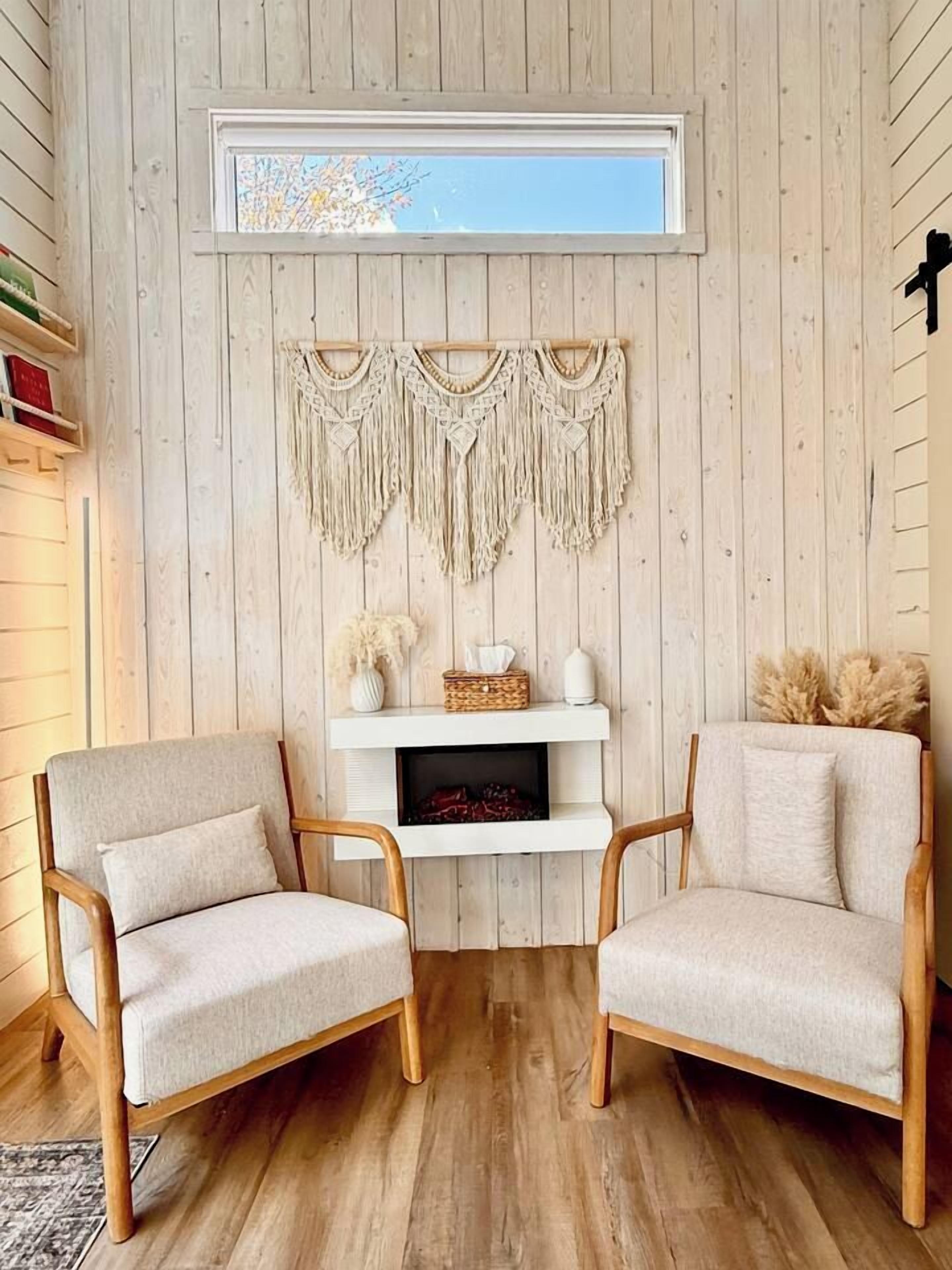 Una stanza con pareti in legno, un camino bianco, due poltrone e una mensola con oggetti decorativi.