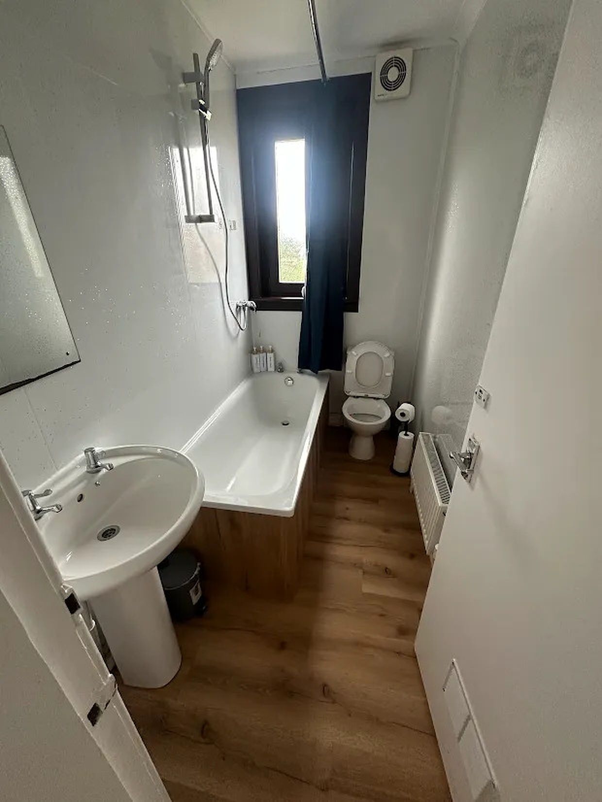 A compact bathroom with a bathtub, sink, toilet, and a window allowing natural light.