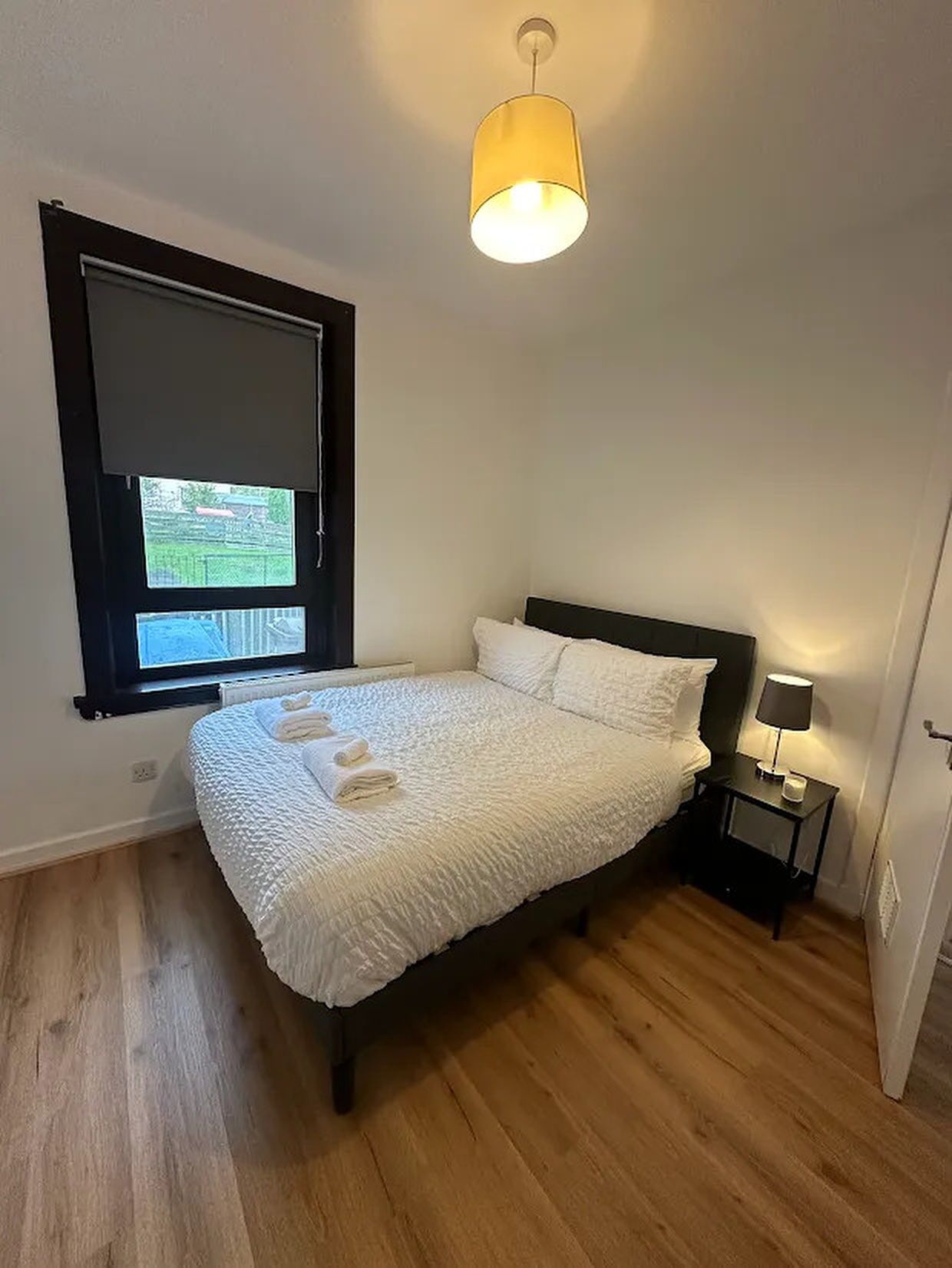 A bedroom with a bed, a nightstand, a lamp, and a window.