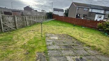A residential backyard with a grassy lawn, a stone pathway, and a wooden fence.