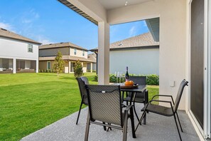 Een terras buiten met een tafel en stoelen, een kleine boom en uitzicht op omliggende huizen.