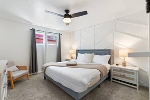 A hotel room with a bed, a chair, a nightstand, a lamp, and a ceiling fan. - PHX | Heated Pool | 10 Min Airport | 18 Scottsdale (Phoenix)