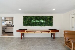 Ein modernes Wohnzimmer mit einer Holzbank, einer grünen Wanddekoration und einem Blick auf eine Küche im Hintergrund.