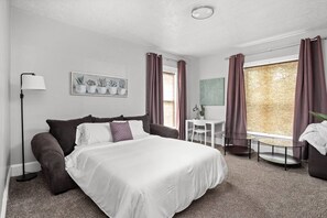 A hotel room with a bed, a desk, a chair, a lamp, and a window with curtains. - The Dingo - Sunny One Bed Apt, Walk to Mass Ave (Indianapolis)