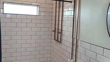 Ein Badezimmer mit Duschkabine, Toilette und Waschbecken, alles in weißen Fliesen.