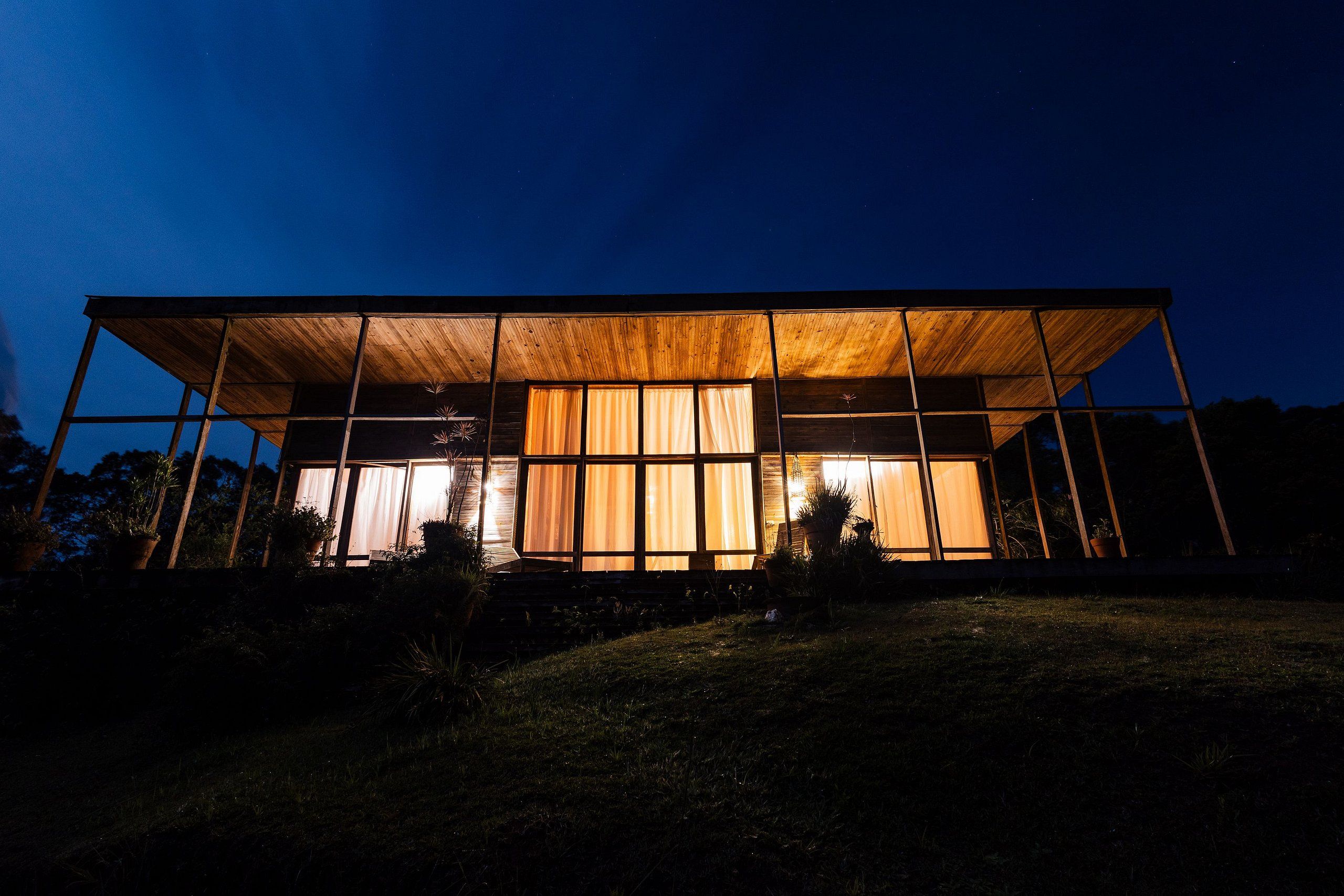 Uma casa moderna com fachada de vidro ampla, estrutura de madeira e cortinas nas janelas.