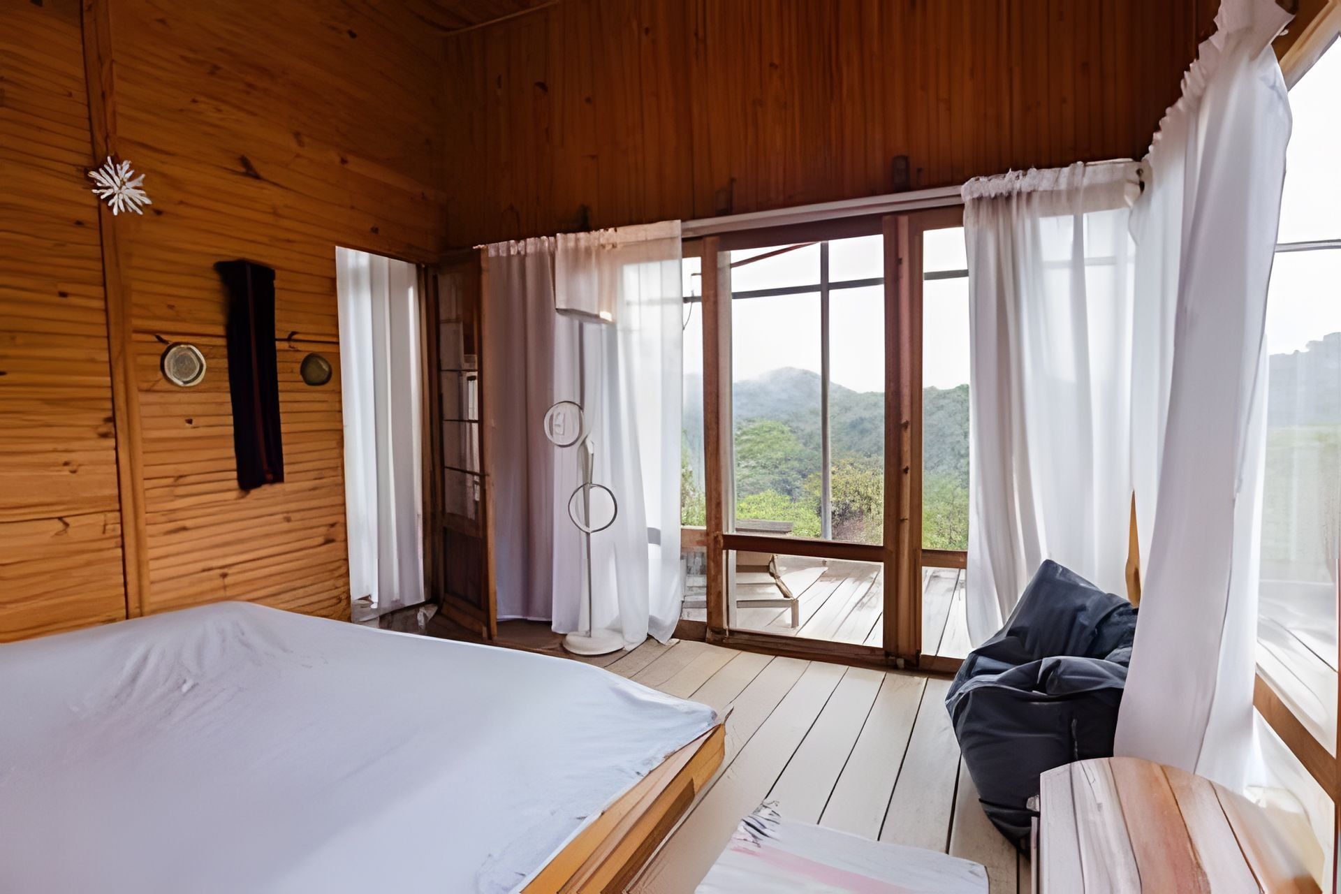 Quarto de cabana de madeira com cama, uma cadeira e vista para o exterior.