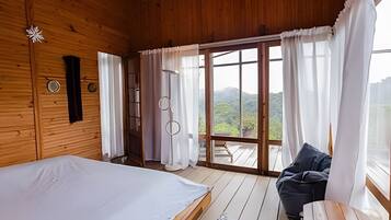 Quarto de cabana de madeira com cama, uma cadeira e vista para o exterior.