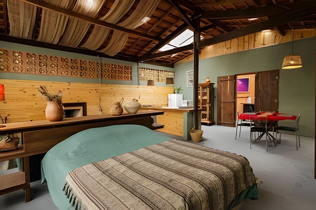 Una habitación rústica con una cama, paredes de madera, una zona de comedor y una cocina.