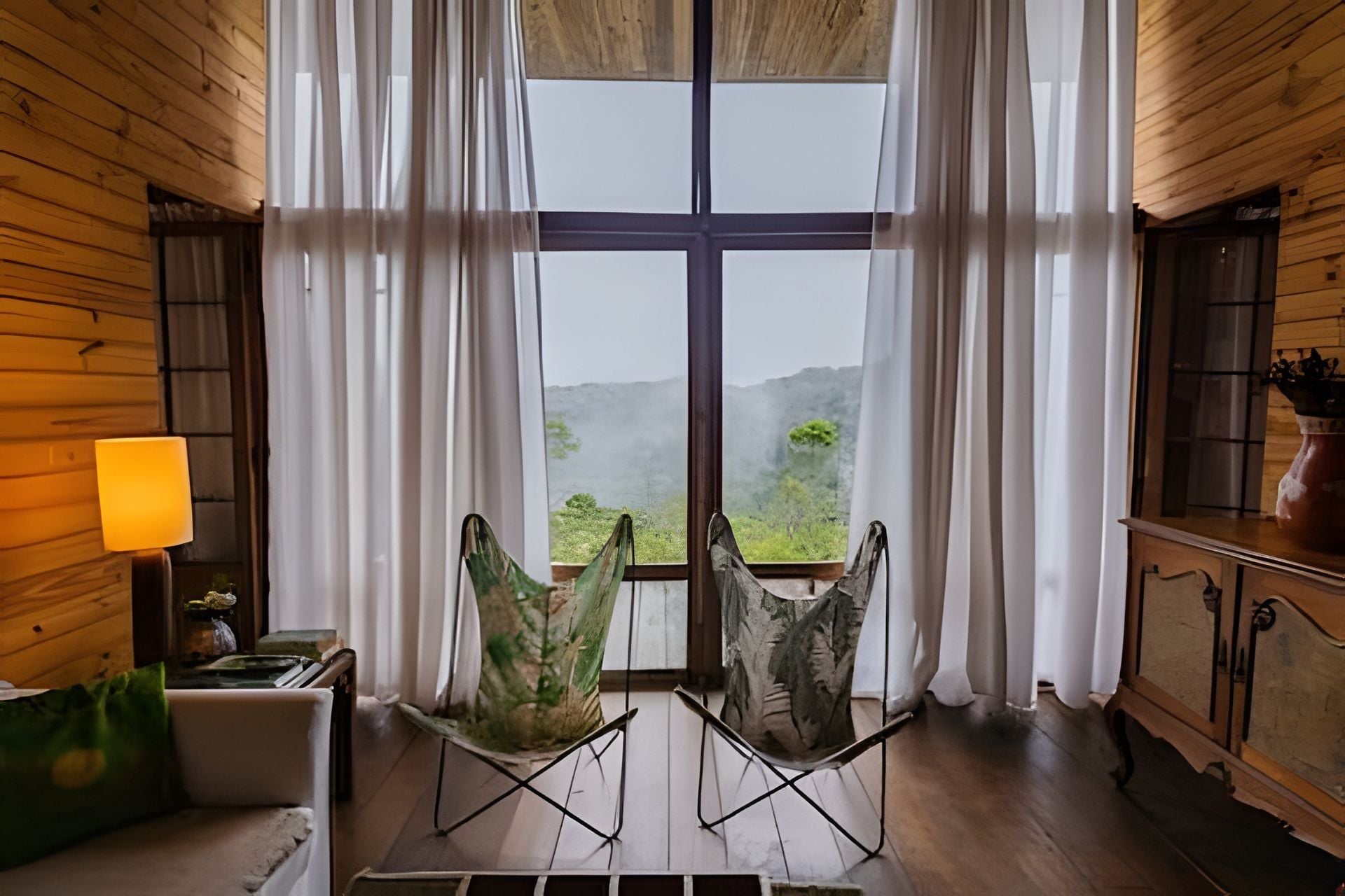 Quarto com uma janela grande, duas cadeiras, um abajur e um armário.