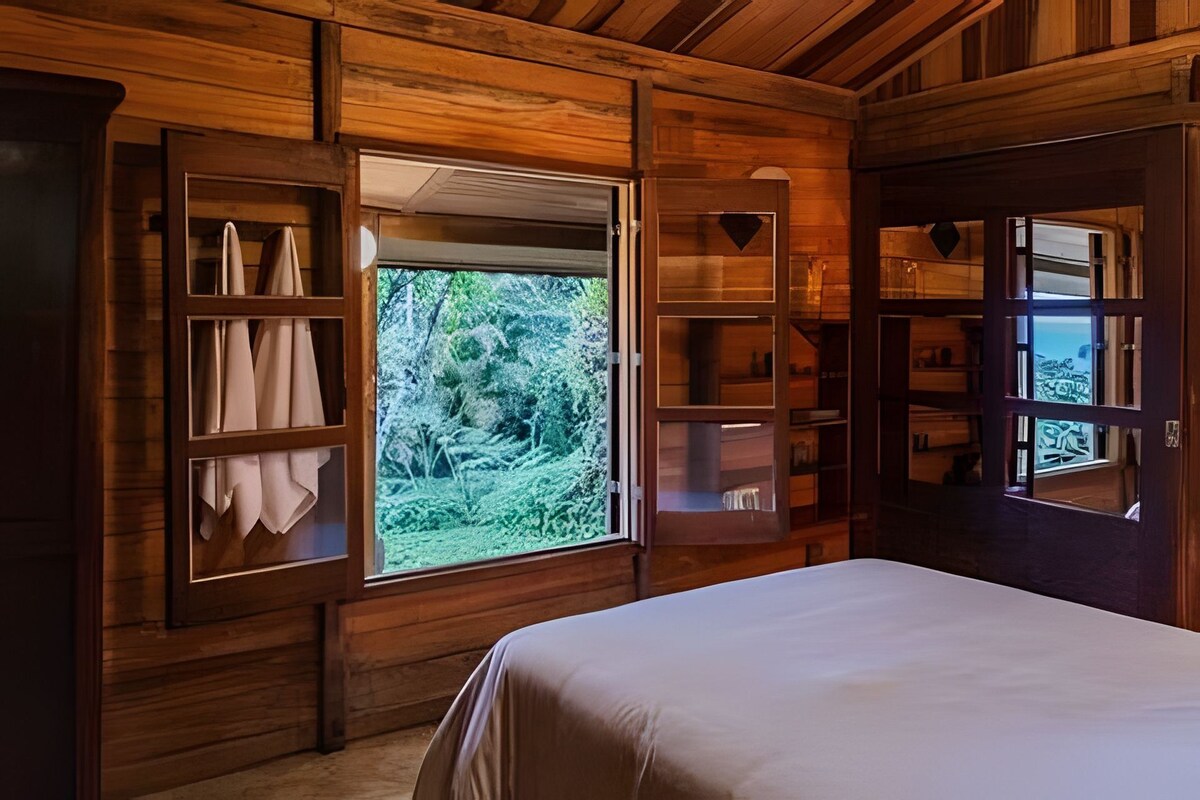 Habitación de cabaña de madera con una cama, estanterías empotradas y una ventana con vista a un bosque.