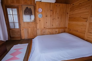 A wooden room with a bed, a window with curtains, a door, and a wall-mounted object. - Macondo uma Vila (Tapirai)