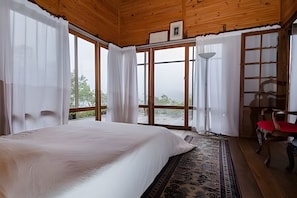 A bedroom with a large bed, a wooden ceiling, and a view through the glass door. - Macondo uma Vila (Tapirai)