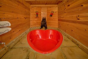 A wooden cabin interior with a heart-shaped bathtub and a bear sculpture. - 2BR Cabin with Hot Tub, Game Room, Wooded Views + Free Tix (Sevierville)