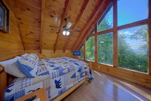 A wooden cabin room with a bed, a ceiling fan, and large windows. - 2BR Cabin with Hot Tub, Game Room, Wooded Views + Free Tix (Sevierville)
