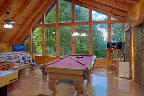 A wooden room with a pool table, a bed with a quilt, and a television. - 2BR Cabin with Hot Tub, Game Room, Wooded Views + Free Tix (Sevierville)