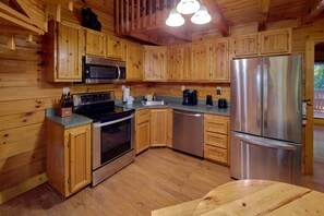 A wooden cabin interior with a kitchen featuring a stainless steel refrigerator, microwave, stove, and dishwasher. - 2BR Cabin with Hot Tub, Game Room, Wooded Views + Free Tix (Sevierville)