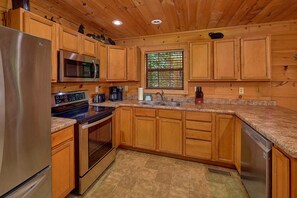 A compact kitchen with wooden cabinets, a stainless steel refrigerator, a microwave, a stove, and a sink. - Mountain Bearadise | Theater, Hot Tub, Game Room, Sleeps 12, Fireplace + Free Attraction Tickets (Sevierville)