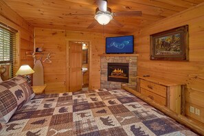 A cozy cabin interior with a fireplace, wooden walls, a ceiling fan, and a television. - Mountain Bearadise | Theater, Hot Tub, Game Room, Sleeps 12, Fireplace + Free Attraction Tickets (Sevierville)