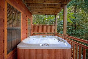 A hot tub on a wooden deck with a wooden railing and a glass door. - Mountain Bearadise | Theater, Hot Tub, Game Room, Sleeps 12, Fireplace + Free Attraction Tickets (Sevierville)