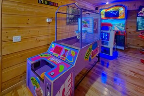 A room with wooden walls, a minigolf game, and a racing game machine. - Mountain Bearadise | Theater, Hot Tub, Game Room, Sleeps 12, Fireplace + Free Attraction Tickets (Sevierville)