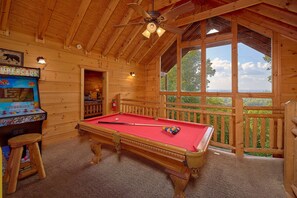 A wooden room with a pool table, a Supercade arcade, and a view through large windows. - Mountain Bearadise | Theater, Hot Tub, Game Room, Sleeps 12, Fireplace + Free Attraction Tickets (Sevierville)
