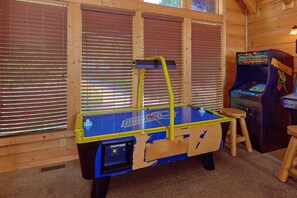 A room with a blue and yellow arcade table, a small stool, and a vintage arcade machine. - Mountain Bearadise | Theater, Hot Tub, Game Room, Sleeps 12, Fireplace + Free Attraction Tickets (Sevierville)