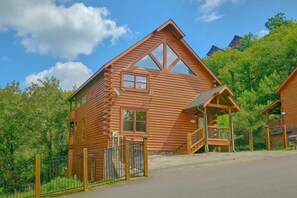 A wooden cabin with a sloped roof, a porch, and a fenced entrance. - Fun Zone | Theater, Hot Tub, Game Room, Sleeps 12, King Suites, Fireplace + Free Attraction Tickets (Sevierville)
