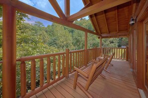 A wooden deck with a railing, benches, and a view of a forested area. - Fun Zone | Theater, Hot Tub, Game Room, Sleeps 12, King Suites, Fireplace + Free Attraction Tickets (Sevierville)
