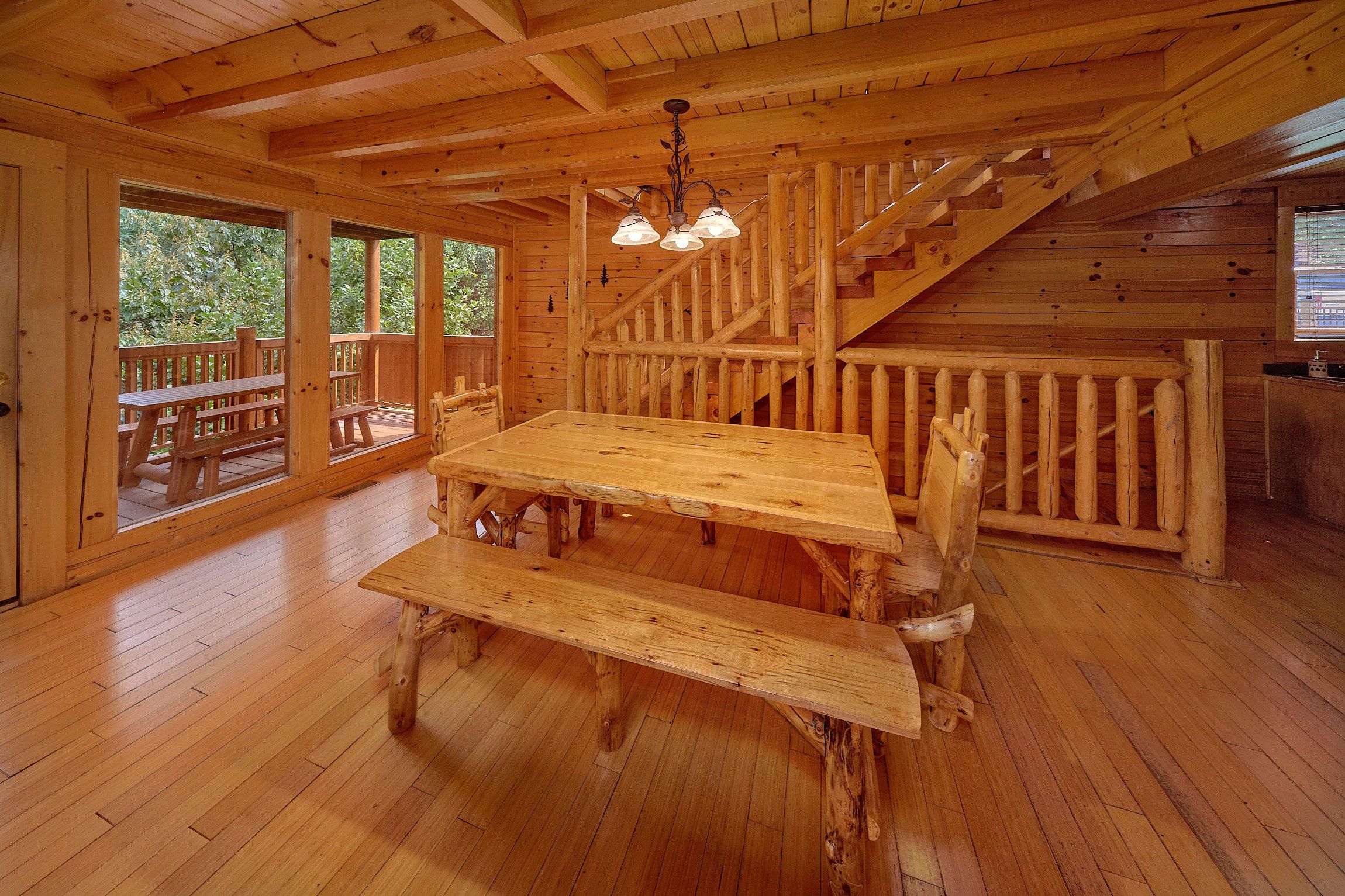 A wooden interior with a dining table and benches, a staircase, and large windows. - Fun Zone | Theater, Hot Tub, Game Room, Sleeps 12, King Suites, Fireplace + Free Attraction Tickets (Sevierville)