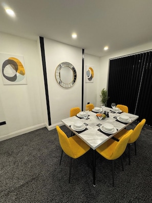 A dining area with a marble table set for four, yellow chairs, and modern wall art. - 3BR Home with Large Garden in Leicester (Leicester)