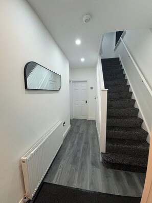 A hallway with a radiator, a mirror, a door, and a staircase. - 3BR Home with Large Garden in Leicester (Leicester)