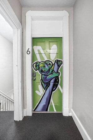 A hallway with a green door featuring a bear illustration, a white door frame, and a carpeted floor. - The Koala - Sunny King Studio -Walk to Mass Ave (Indianapolis)