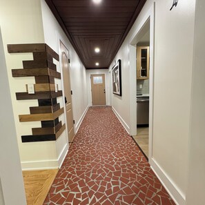 Un passadís amb un paviment estampat, una làmpada penjada a la paret i una porta al final.