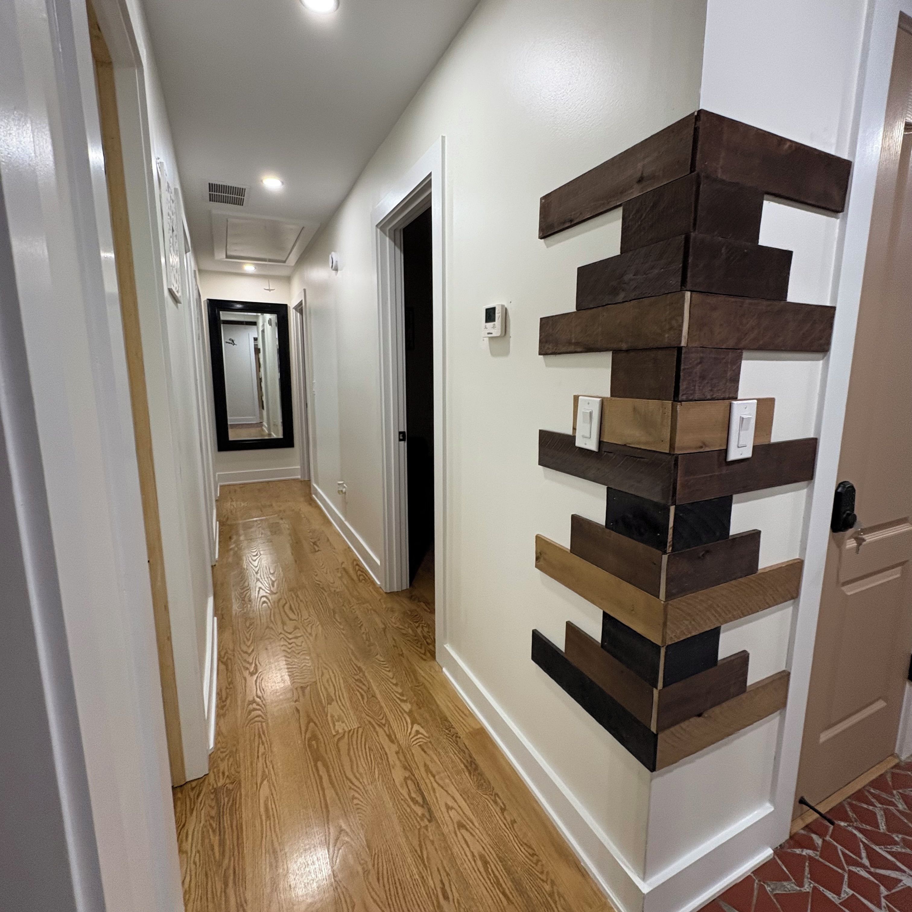A hallway with wooden flooring, white walls, and a decorative wall panel.