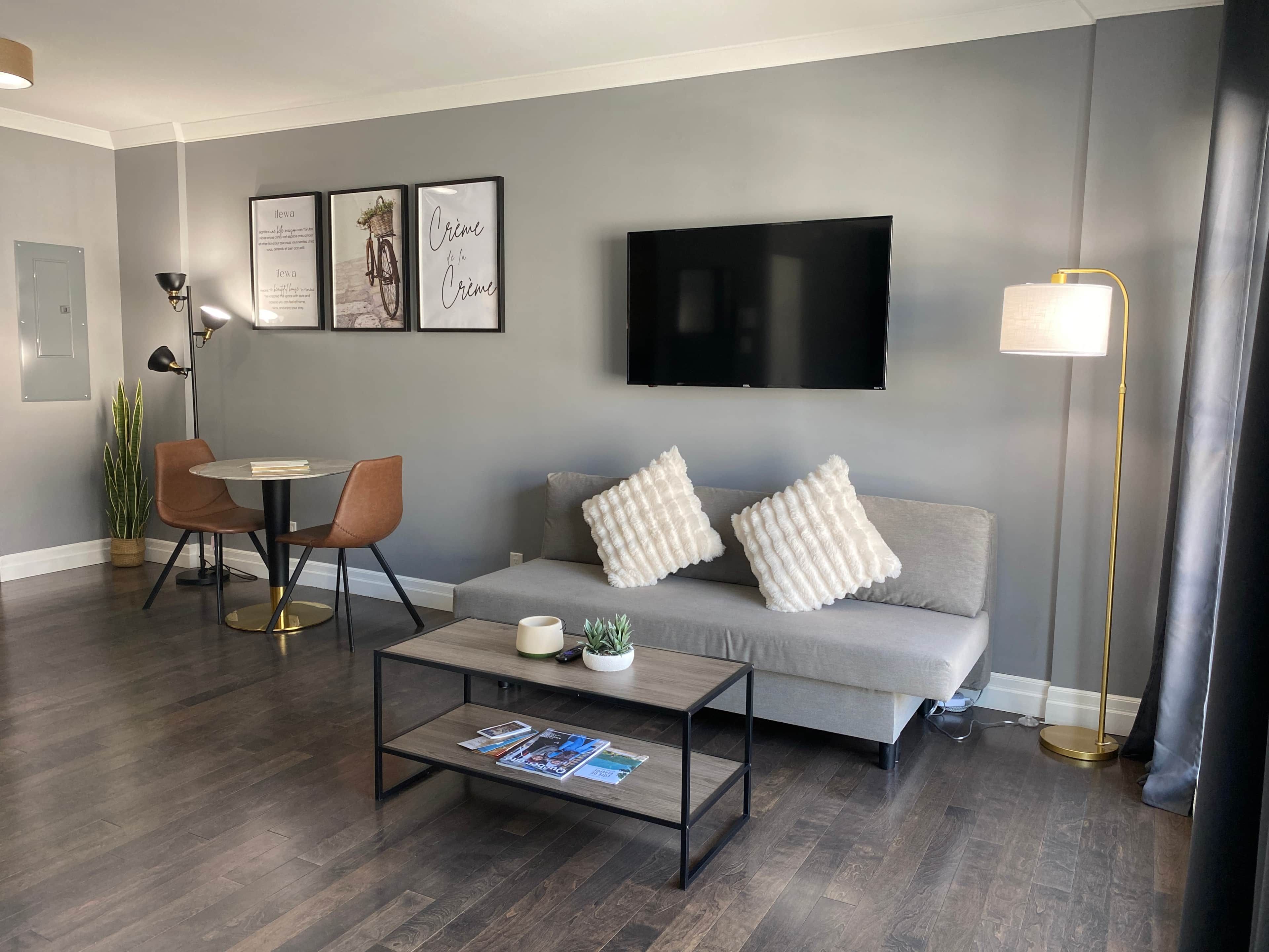 Una sala de estar moderna con un sofá gris, una mesa de centro, un televisor montado en la pared y una lámpara de pie.