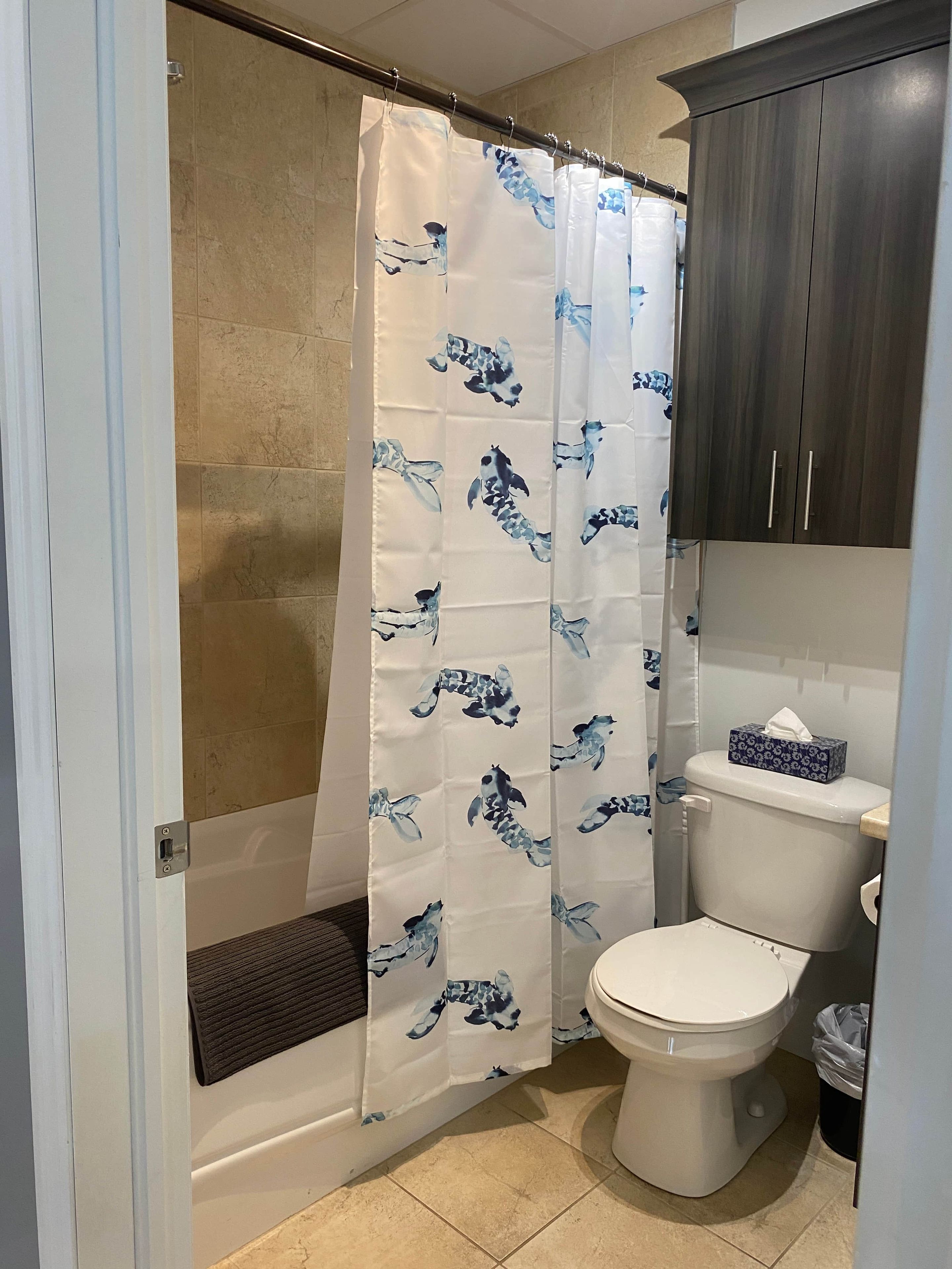 Un baño con cortina de ducha estampada con un motivo de carpas, un inodoro y un mueble de madera oscura.