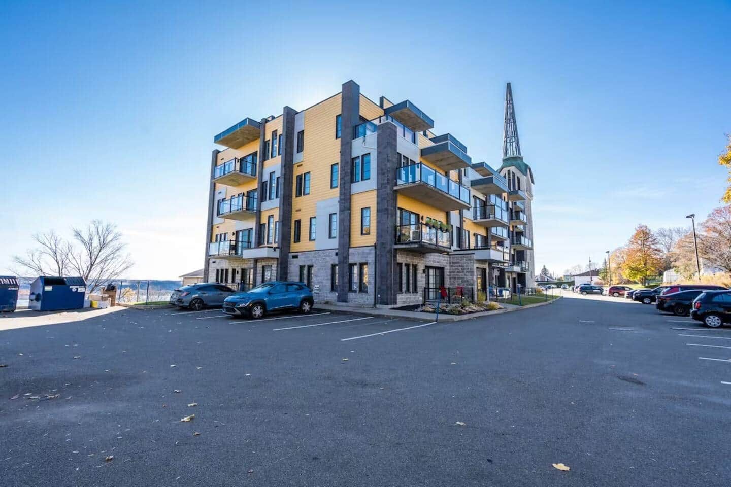 A multi-story residential building with balconies, a parking lot, and a distant church spire.