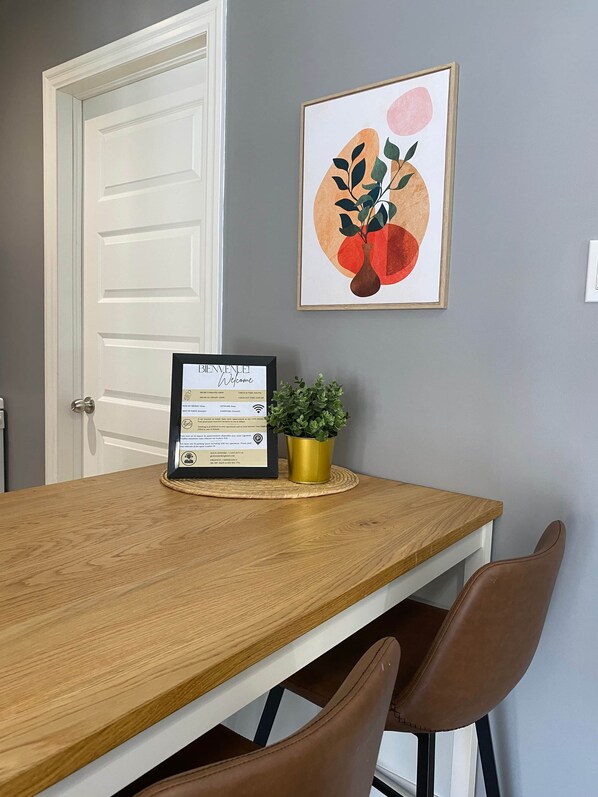 Une table de salle à manger en bois, agrémentée d’un panneau d’accueil encadré, d’une plante en pot et d’une œuvre d’art accrochée au mur.