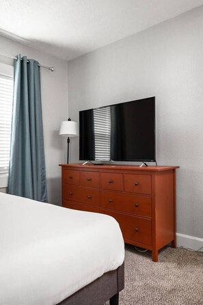 A hotel room with a bed, a wooden dresser, a flat-screen TV, and a lamp. - The Kangaroo - Bright Studio Apt, Walk to Mass Ave (Indianapolis)